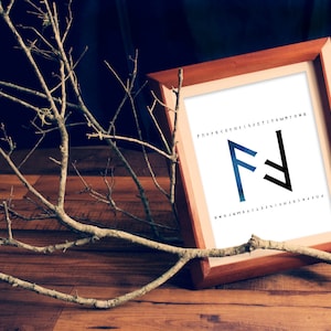 May include: A wooden frame with a white background and a black and blue rune symbol. The rune symbol is surrounded by a circle of letters. The frame is sitting on a wooden surface with a branch of a tree in the foreground.