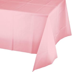 May include: A light pink rectangular tablecloth. The tablecloth is made of a thin, opaque material and is folded, creating visible creases. The fabric drapes over the edge of a table, with the corner of the tablecloth hanging down.