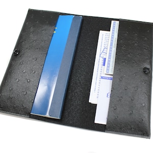 May include: Black leather folder with a blue notebook and some papers inside. The folder has a textured, ostrich-like pattern and two black snap buttons.