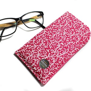 May include: A pink and white patterned glasses case with a white logo that says "Kipapee Designs".