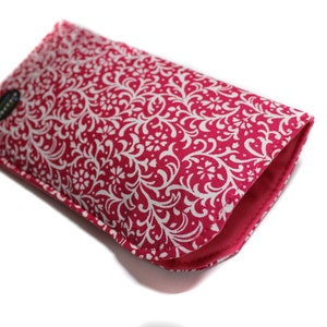 May include: A pink and white patterned phone case with a white floral design. The case is made of fabric and has a soft, padded lining.