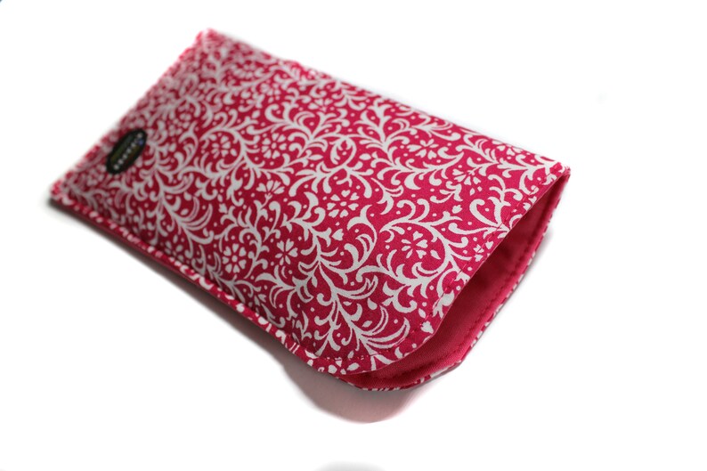 May include: A pink and white patterned phone case with a white floral design. The case is made of fabric and has a soft, padded lining.