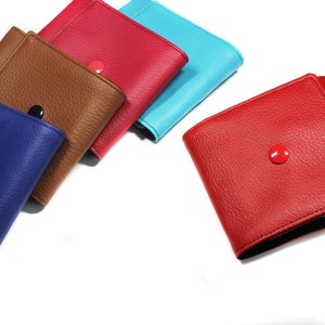 May include: Five square wallets with a textured surface, each featuring a matching colored snap button closure. The wallets are arranged in a row and come in blue, brown, pink, light blue, and red, each with a distinct snap button color.