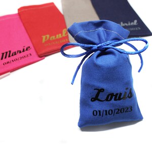 Puede incluir: Bolsa de regalo de tela azul con cierre de cordón. La bolsa está personalizada con el nombre "Louis" y la fecha "01/10/2023".