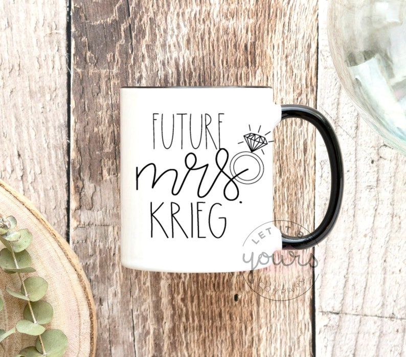 May include: White ceramic mug with a black handle. The mug has black text that reads "Future Mrs. Krieg" with a diamond ring illustration.