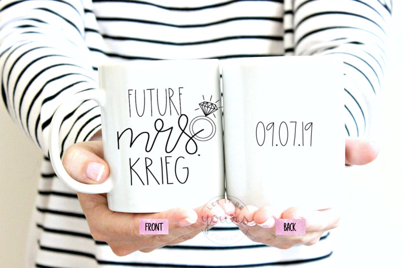 May include: White ceramic mug with black text that reads "Future Mrs. Krieg" and a diamond ring illustration on the front. The back of the mug has the date "09.07.19" written in black.