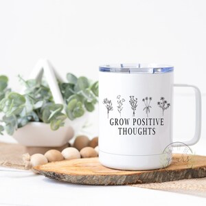 May include: White stainless steel travel mug with a black outline of flowers and the text "Grow Positive Thoughts".