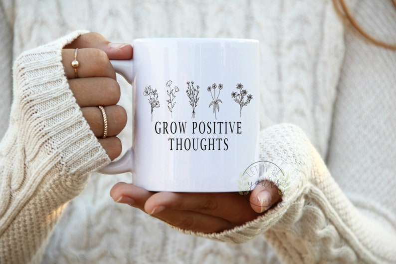 May include: White ceramic mug with a black outline of five flowers and the text "GROW POSITIVE THOUGHTS".