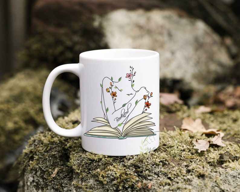 Pu&ograve; includere: Tazza in ceramica bianca con un disegno a linea nera di una persona che legge un libro con fiori che crescono dal suo corpo. Il testo "Bookfriend" &egrave; scritto sul libro.