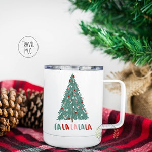 May include: White travel mug with a green Christmas tree and red and pink ornaments. The text "Fa La La La La" is printed below the tree.