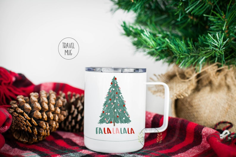 May include: White travel mug with a green Christmas tree and red and pink ornaments. The text "Fa La La La La" is printed below the tree.