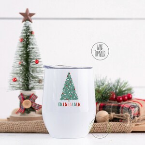 May include: White stainless steel wine tumbler with a green Christmas tree design and the text "Fa la la la la" in red, pink, and green.