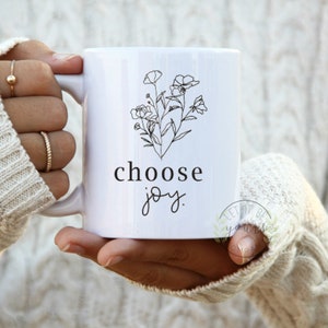 May include: White ceramic mug with a black line drawing of flowers and the text "choose joy".
