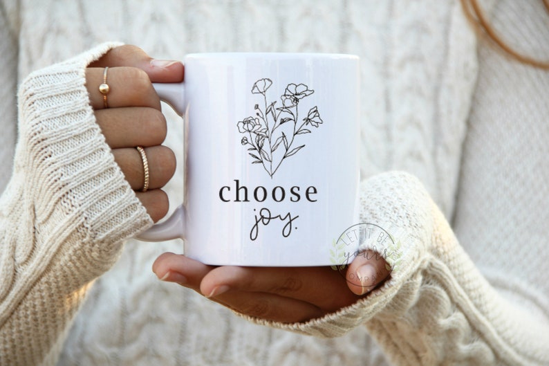 May include: White ceramic mug with a black line drawing of flowers and the text "choose joy".