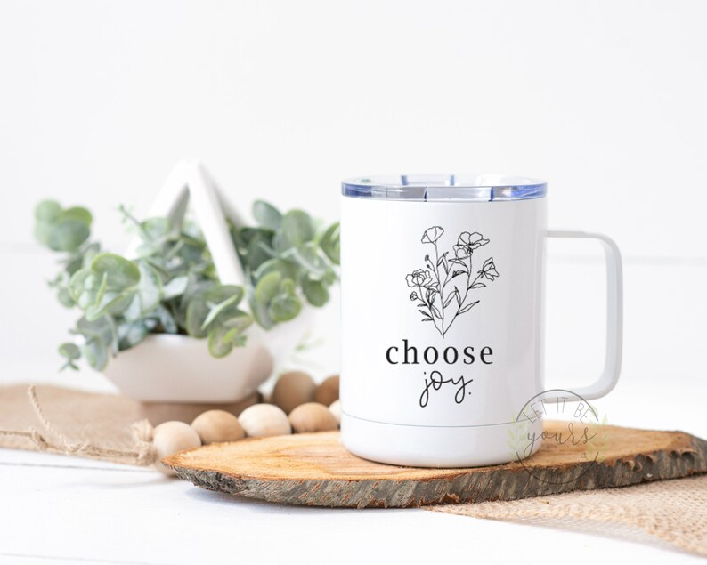 May include: White stainless steel travel mug with a black floral design and the text "choose joy".