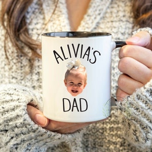 Peut inclure: Une tasse en c&eacute;ramique blanche avec un bord et une poign&eacute;e noirs. La tasse pr&eacute;sente une photo d'une jeune fille avec un n&oelig;ud dans les cheveux et le texte "Alivia's Dad" imprim&eacute; dessus.
