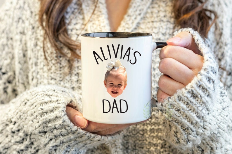 Peut inclure: Une tasse en c&eacute;ramique blanche avec un bord et une poign&eacute;e noirs. La tasse pr&eacute;sente une photo d'une jeune fille avec un n&oelig;ud dans les cheveux et le texte "Alivia's Dad" imprim&eacute; dessus.