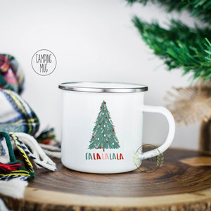 May include: White enamel camping mug with a green Christmas tree and the text "Fa La La La La" printed on it. The mug has a silver rim.
