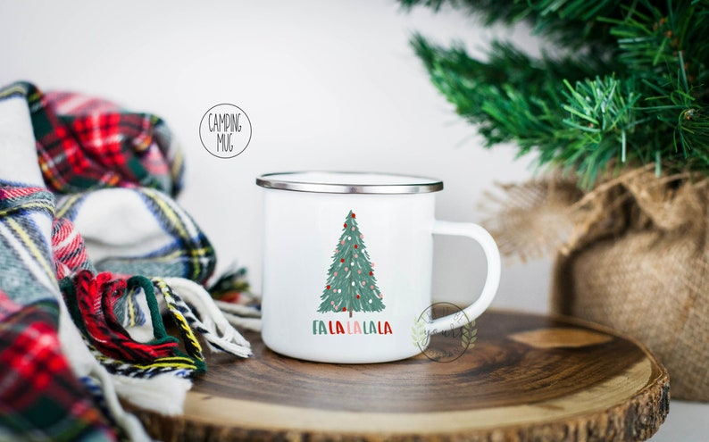 May include: White enamel camping mug with a green Christmas tree and the text "Fa La La La La" printed on it. The mug has a silver rim.