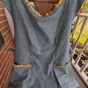 May include: A blue and yellow floral print apron with two pockets and a ruffled neckline.