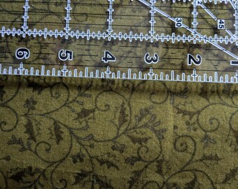 May include: A clear, transparent ruler with white markings and numbers is positioned over a green fabric with a dark floral pattern. The ruler is marked in inches, with numbers from 1 to 7 visible.