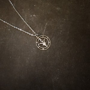 Peut inclure: Un collier en argent avec un pendentif circulaire représentant un motif stylisé d'une fleur avec un centre pointu. Le pendentif est orné de chiffres romains sur le bord.