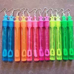 May include: Ten colorful plastic bubble wands with star-shaped charms hanging from silver hooks. The wands are filled with clear bubble solution and have a small brush at the end.