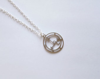 May include: A silver necklace with a circular pendant featuring a stylized symbol with a cross and a crescent moon.