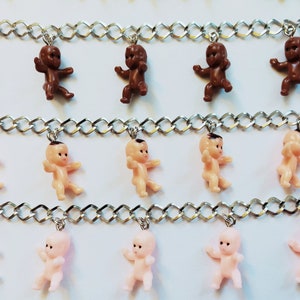 May include: Three silver chains with baby doll charms. The top chain has brown baby dolls, the middle chain has nude baby dolls, and the bottom chain has pink baby dolls.