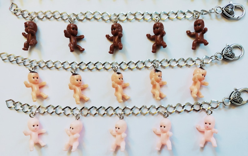 May include: Three silver chains with baby doll charms. The top chain has brown baby dolls, the middle chain has nude baby dolls, and the bottom chain has pink baby dolls.
