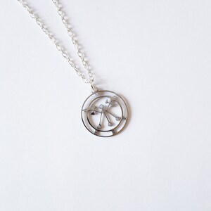 May include: A silver necklace with a circular pendant featuring a geometric design. The pendant has a central circle with radiating lines and smaller circles at the ends.