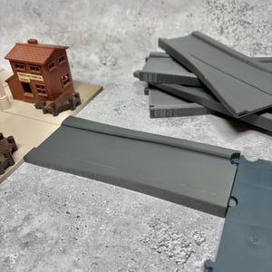 May include: A set of grey plastic train track pieces. The track pieces are designed to connect together to create a train track layout. The track pieces are made of a durable plastic and are suitable for use with toy trains.