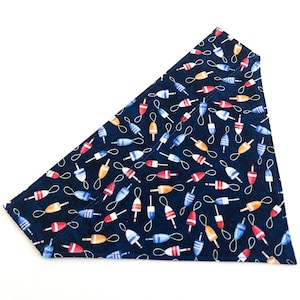 May include: A navy blue dog bandana with a pattern of red, white, and yellow buoys. The bandana is triangular in shape and has a white border.