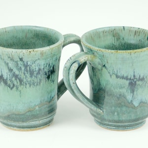 May include: Two handmade ceramic mugs with a green and blue glaze. The mugs have a unique, hand-thrown look and feel.