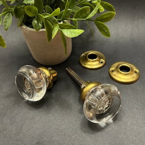 以下が含まれることがあります： 真鍮製のベースと真鍮製のバックプレートが付いた、透明なガラス製のドアノブ2個。ノブはファセットデザインです。