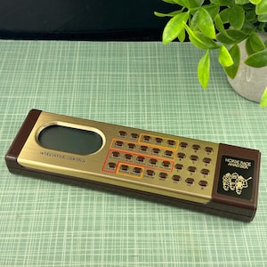 Può includere: Un computer portatile vintage oro e marrone "Horse Race Analyzer". Il dispositivo ha una forma rettangolare con numerosi pulsanti e un piccolo schermo. Il testo "HANDICAPPING COMPUTER" è stampato sul dispositivo.