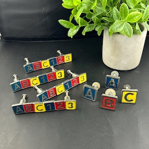 Op de afbeelding: Een verzameling kleurrijke kastknoppen met de letters A, B en C en de cijfers 1, 2 en 3. De knoppen zijn rechthoekig met een zilverkleurige metalen basis en zijn rood, geel en blauw.