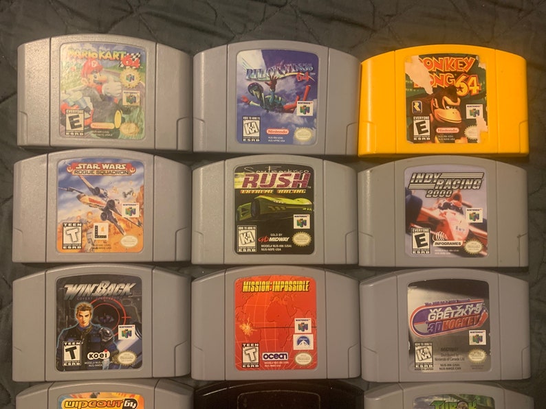 May include: A collection of 11 Nintendo 64 game cartridges, including titles like "Mario Kart 64", "Star Wars: Rogue Squadron", "Donkey Kong 64", and "Indy Racing 2000".