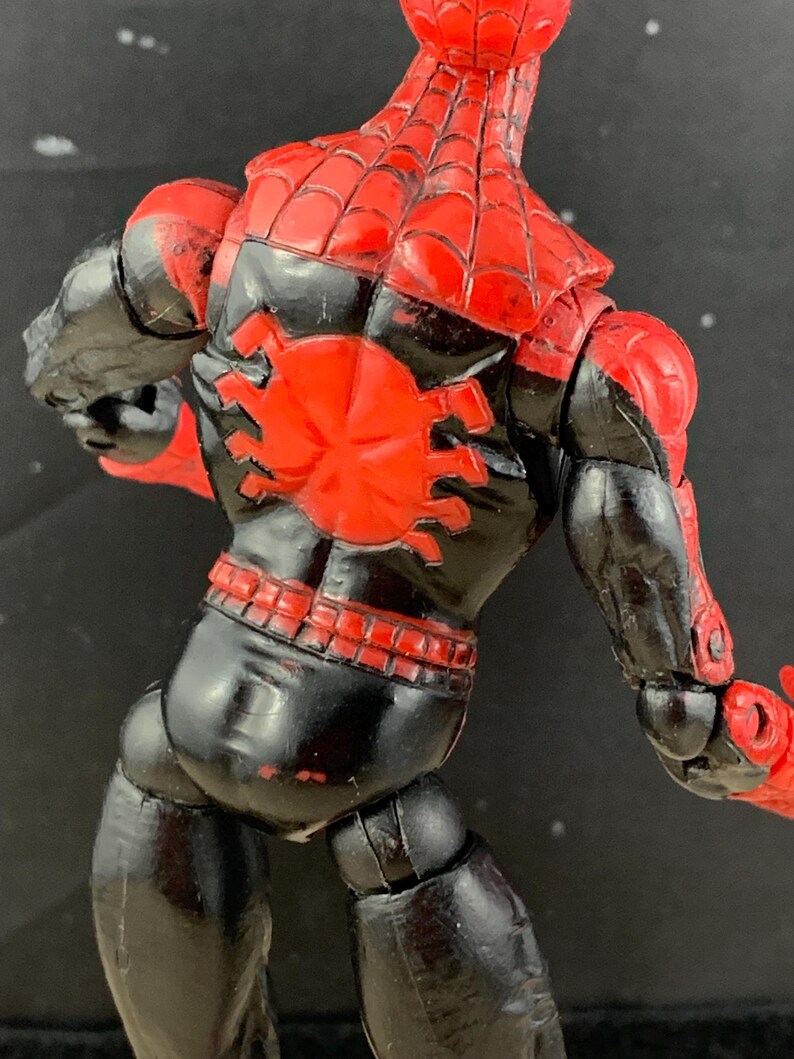 K&ouml;nnte beinhalten: Rote und schwarze Actionfigur eines Superhelden, von hinten gesehen. Die Figur hat ein rotes Spinnennetz-Design auf Kopf und Schultern sowie ein gro&szlig;es rotes Spinnenemblem auf dem R&uuml;cken. Der K&ouml;rper ist schwarz mit roten Akzenten.