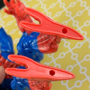 Peut inclure: Gros plan sur une figurine de Spider-Man. La figurine est principalement bleue et rouge, avec le motif de toile d'araign&eacute;e visible. Les mains de la figurine sont rouges, et le texte "1996 MARVEL MADE IN CHINA" et "TOY BIZ, INC." sont visibles.