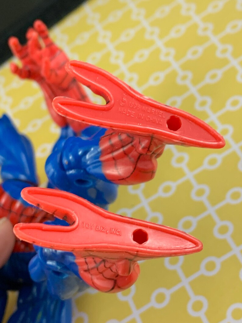 Peut inclure: Gros plan sur une figurine de Spider-Man. La figurine est principalement bleue et rouge, avec le motif de toile d'araign&eacute;e visible. Les mains de la figurine sont rouges, et le texte "1996 MARVEL MADE IN CHINA" et "TOY BIZ, INC." sont visibles.