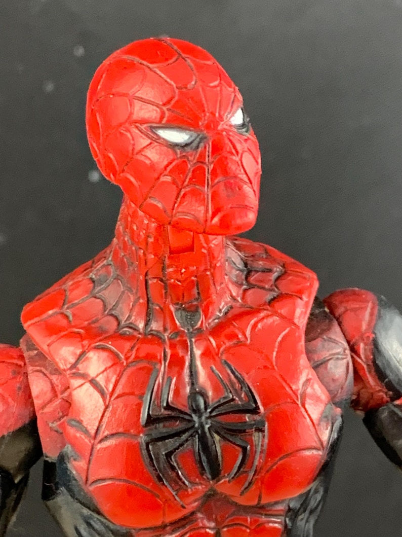 K&ouml;nnte beinhalten: Nahaufnahme einer rot-schwarzen Spider-Man-Actionfigur. Die Figur hat einen roten Kopf mit wei&szlig;en Augen und ein schwarzes Spinnennetz-Design. Die Brust zeigt ein schwarzes Spinnenemblem. Die Figur ist ein Sammlerspielzeug.