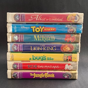 May include: A stack of eight VHS tapes featuring classic Disney animated films, including "Alice in Wonderland", "Toy Story", "The Little Mermaid", "The Lion King", "A Bug's Life", "101 Dalmatians", and "The Jungle Book".
