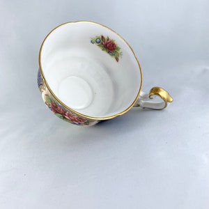 May include: A white teacup with a floral pattern in shades of pink, blue, and green. The cup has a gold rim and a gold handle.
