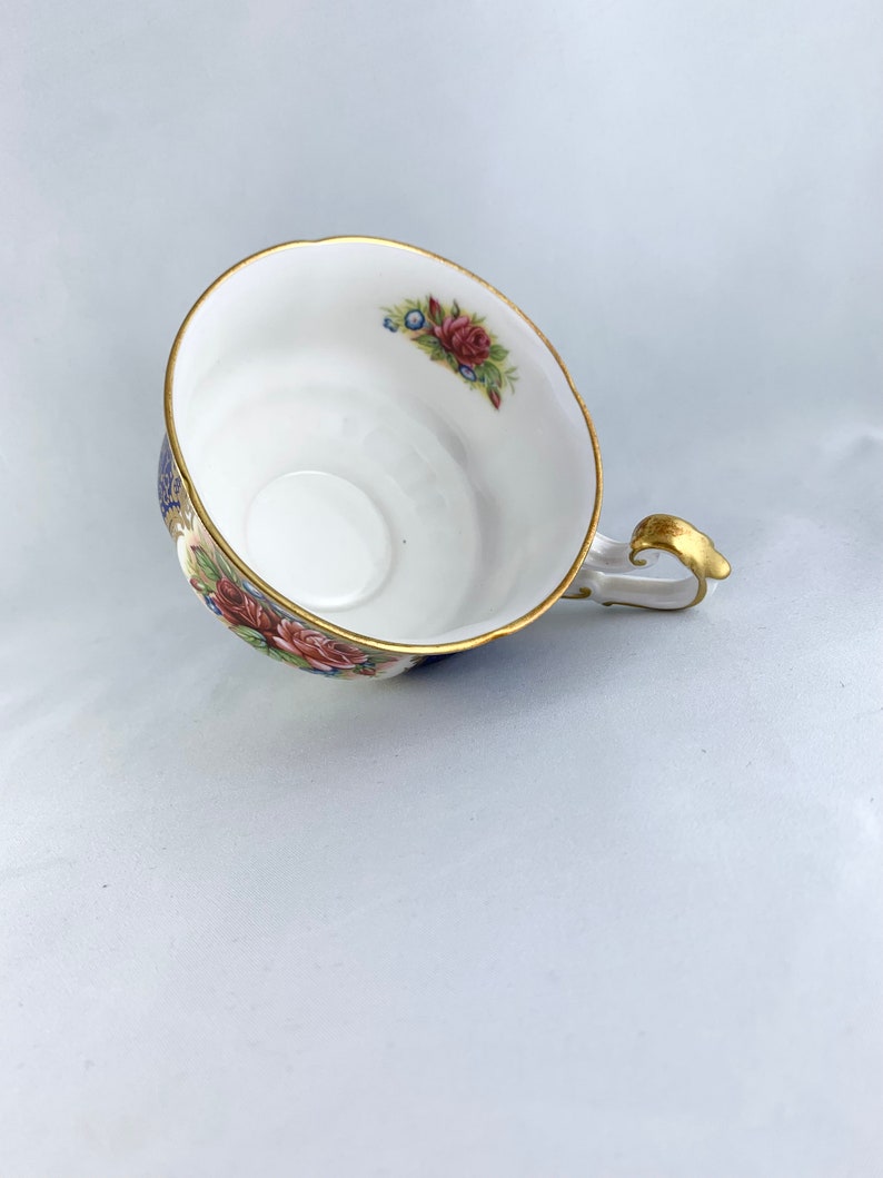 May include: A white teacup with a floral pattern in shades of pink, blue, and green. The cup has a gold rim and a gold handle.