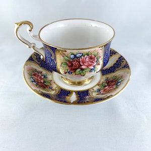 May include: A blue and gold teacup and saucer set with a floral design. The cup and saucer are decorated with a pink and red rose pattern.