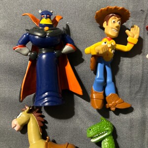 Pu&ograve; includere: Una collezione di statuette dei personaggi di Toy Story, tra cui Zurg con mantello blu e arancione, Woody con cappello da cowboy, un cavallo e un dinosauro verde. I giocattoli sono in plastica e dai colori vivaci.