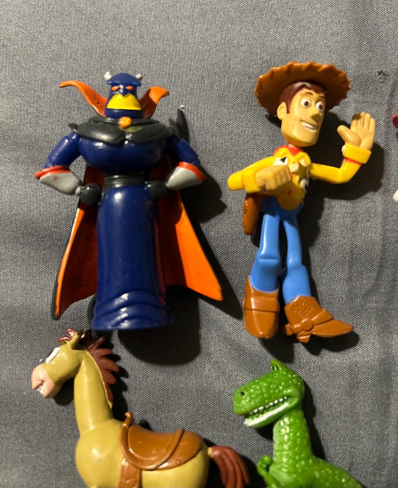 Pu&ograve; includere: Una collezione di statuette dei personaggi di Toy Story, tra cui Zurg con mantello blu e arancione, Woody con cappello da cowboy, un cavallo e un dinosauro verde. I giocattoli sono in plastica e dai colori vivaci.