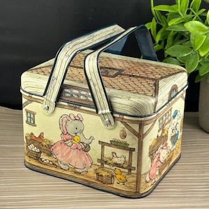 Può includere: Cestino da picnic vintage in metallo con una scena di fattoria stravagante con un elefante in un vestito rosa, pulcini e galline. Il cestino ha un design a tetto in legno e un manico blu. La combinazione di colori è beige, marrone e pastello.