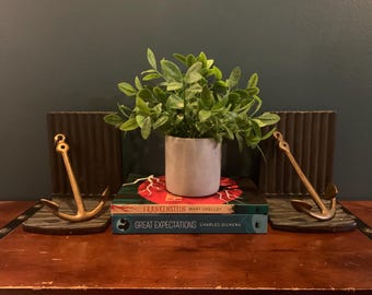 May include: A decorative display featuring a small potted plant, two books, and two anchor-shaped bookends. The books are titled "Frankenstein" and "Great Expectations." The bookends and anchors are gold-colored.